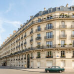 Immeuble haussmannien en pierre de taille à l'angle d'une rue parisienne avec une voiture ancienne garée devant.